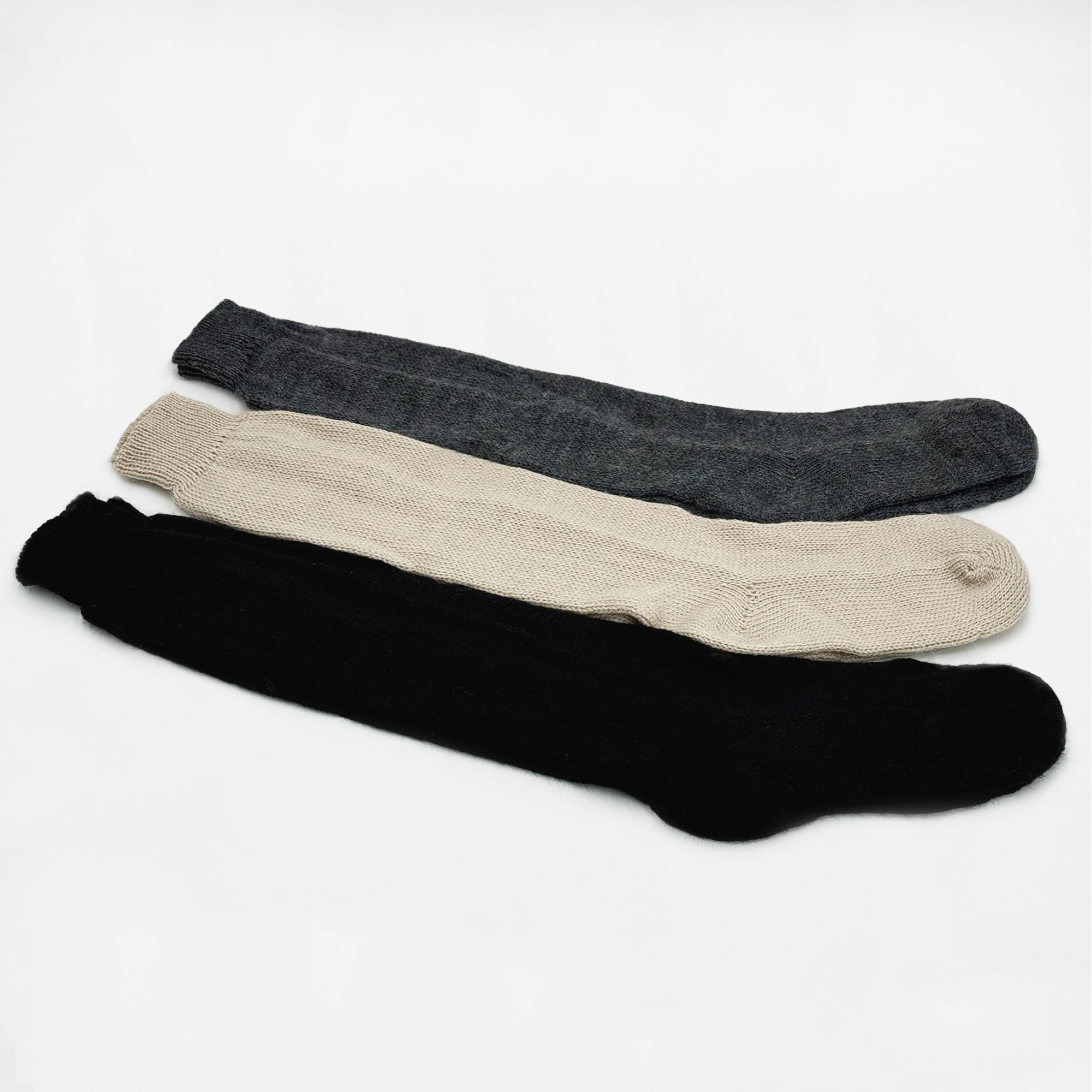 Three woolen knee-length socks are laid flat. They are dark gray, beige, and black, displayed against a plain white background, showcasing texture and color contrast.