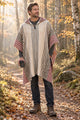 Man wearing the cream and burgundy striped llama wool hooded poncho on a woodland path with a coffee