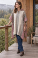 Woman in the cream and burgundy striped hooded poncho with jeans on a wooden terrace