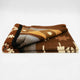A folded blanket with geometric patterns in brown, tan, gray, and cream hues rests on a white surface, showing a southwestern-inspired design.