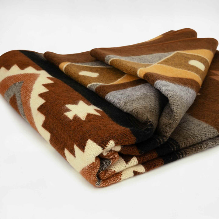 A folded blanket displays a geometric pattern in brown, beige, and gray tones, featuring zigzag and star motifs, placed against a plain white background.