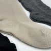 Beige, grey, and black woolen socks are lying flat, side by side, on a white surface, showcasing their knit texture and subtle color contrast.