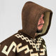 Clint Eastwood alpaca wool poncho – a person wears a brown hooded poncho with geometric patterns, looking to the side. The background is plain and neutral
