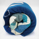 A rolled blanket with geometric patterns in blue, teal, and cream colors rests against a plain white background.