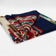 A colorful, folded wool blanket displays intricate red, blue, and beige patterns on a plain white background.