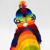 A colorful knitted figure displays vibrant rainbow-striped patterns. The figure features a hat with tassels on top and wrapped fabric resembling a scarf, against a plain white background.