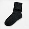 A single black sock lies flat against a plain, light gray background, showcasing its ribbed texture and classic ankle-high design.