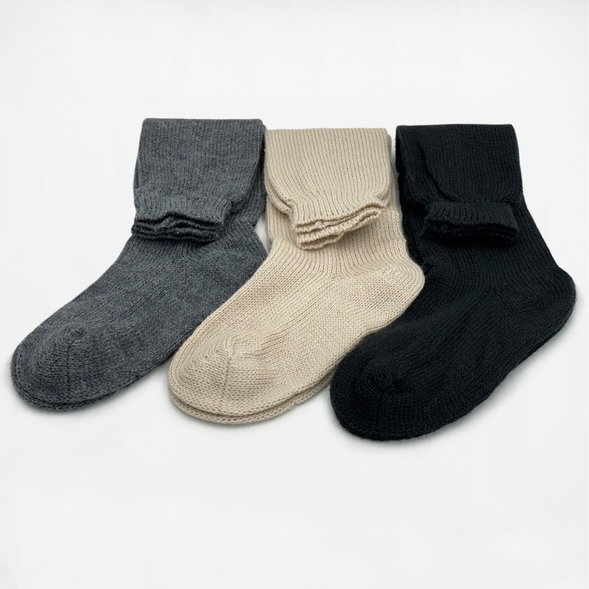 Three knit socks lie flat side by side; one gray, one beige, one black, on a plain white background.