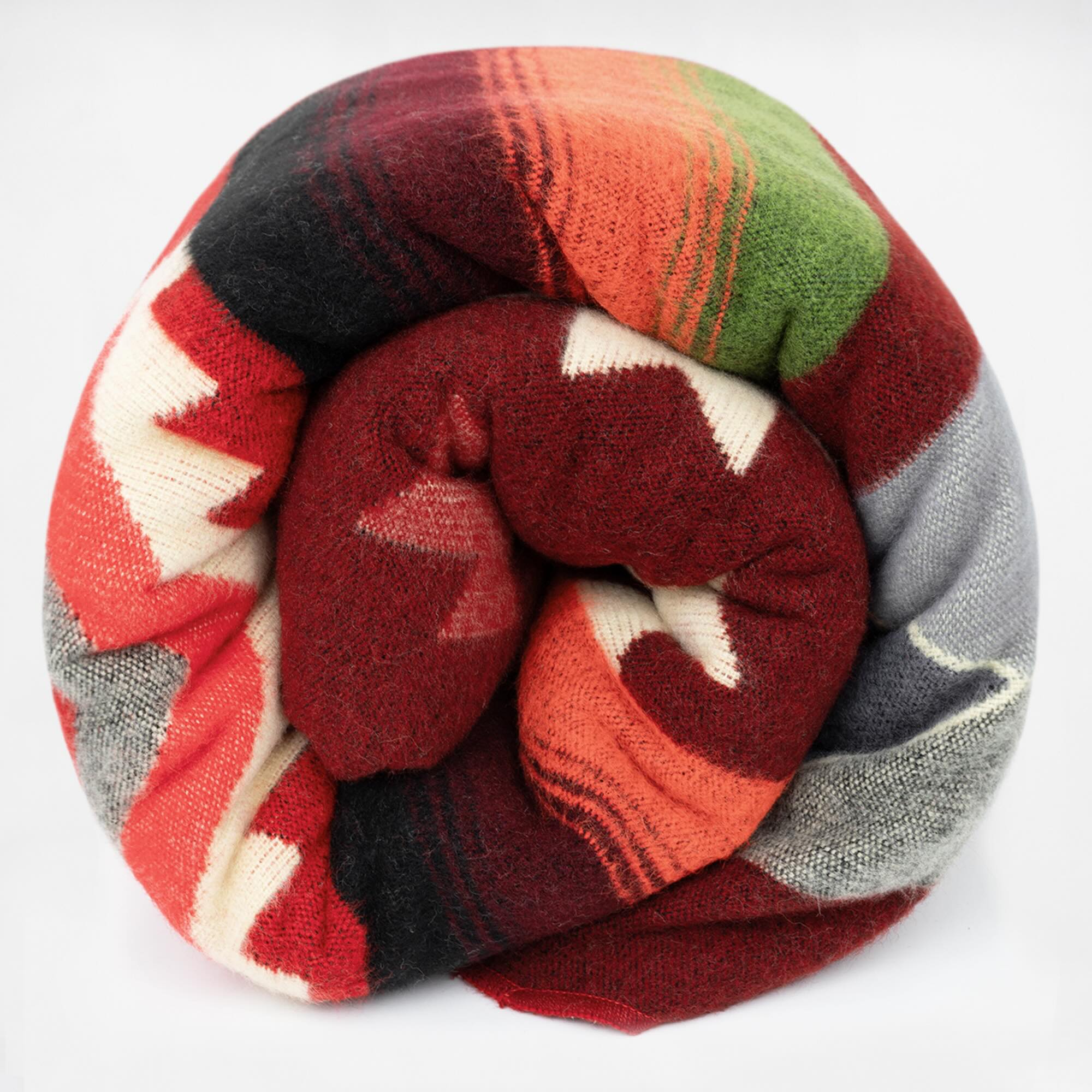 A multicolored blanket, featuring red, green, orange, and gray patterns, is tightly rolled. It is displayed against a plain white background.