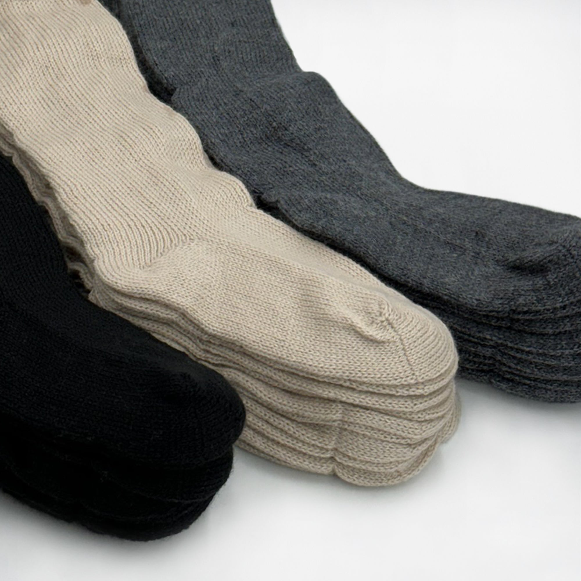 Three stacks of knit socks lie flat; each stack is a different color: black, beige, and gray. They are neatly arranged against a plain white background.