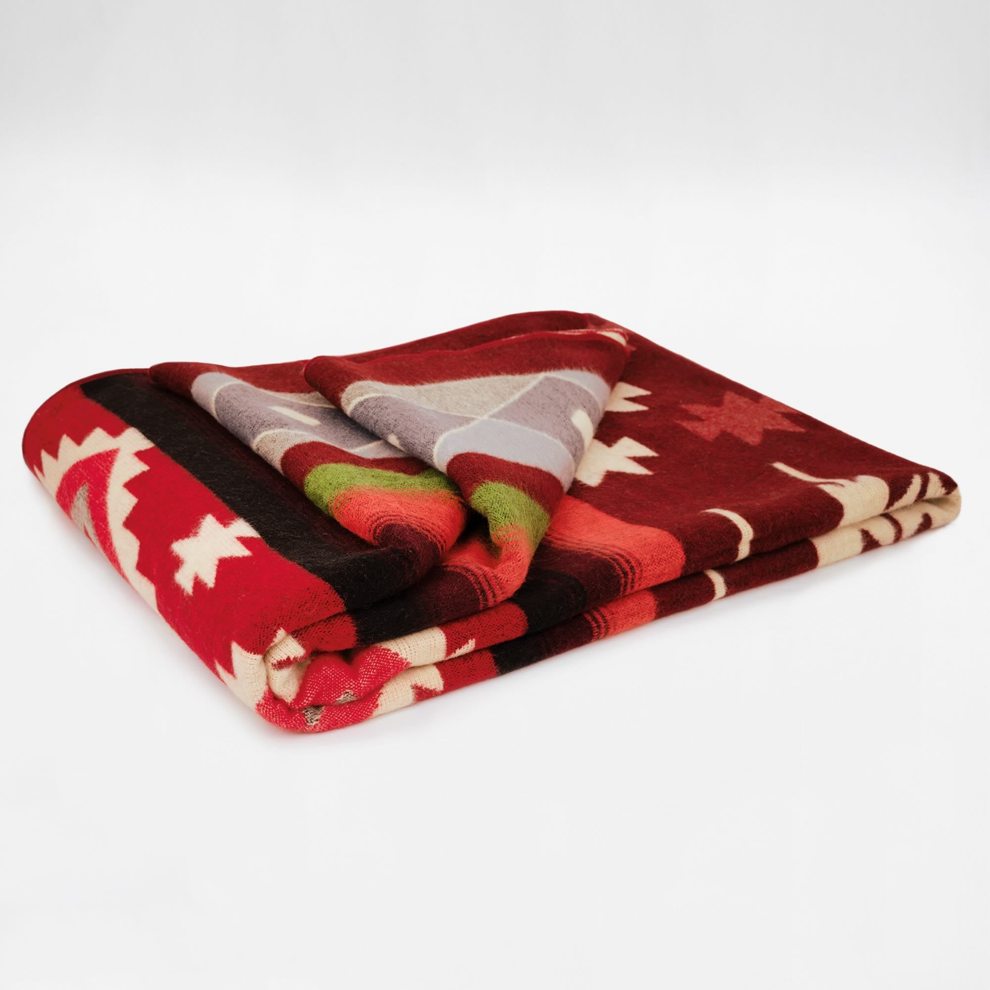 A colorful, folded blanket lies on a flat surface. It features geometric patterns in red, white, green, and gray, creating an intricate design against a plain white background.