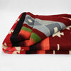 A folded woolen blanket displays a Southwest-inspired geometric pattern in red, green, gray, and black. It rests on a plain white background, highlighting its vibrant design.