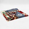 A folded blanket features intricate geometric patterns in red, blue, and cream colors, lying on a plain white background.