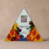 A triangular chocolate packaging with vibrant, colorful cacao illustrations. Text reads: ECUADOR, 100 x 100, and Flavors that brighten the day CHOCOLATE. Set against a soft beige background.