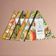 Triangular chocolate boxes featuring colorful, botanical illustrations are lined up against a pinkish background. Text on the front reads: kamm CHAI TEA 85% CACAO SUGAR FREE.