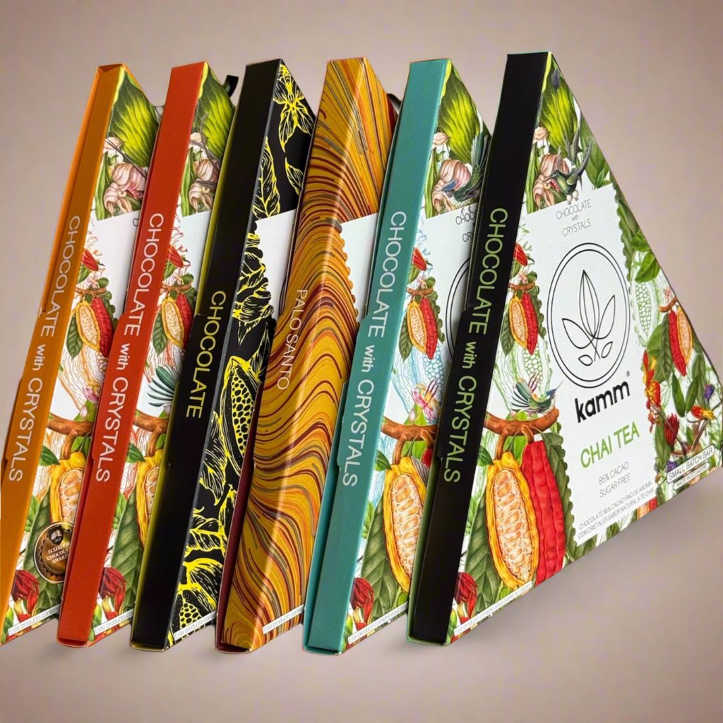 Chocolate bars arranged in a row, showcasing colorful, artistic packaging with botanical designs. Text includes: CHOCOLATE with CRYSTALS, PALO SANTO, kamm, CHAI TEA, 81% CACAO, SUGAR FREE.