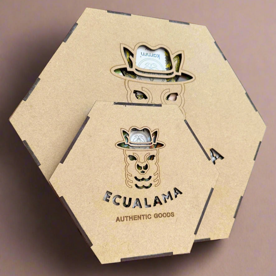 Hexagonal wooden boxes feature a llama face cutout wearing a hat, revealing colorful contents. The text reads Ecualama AUTHENTIC GOODS. The boxes rest on a flat, neutral surface.