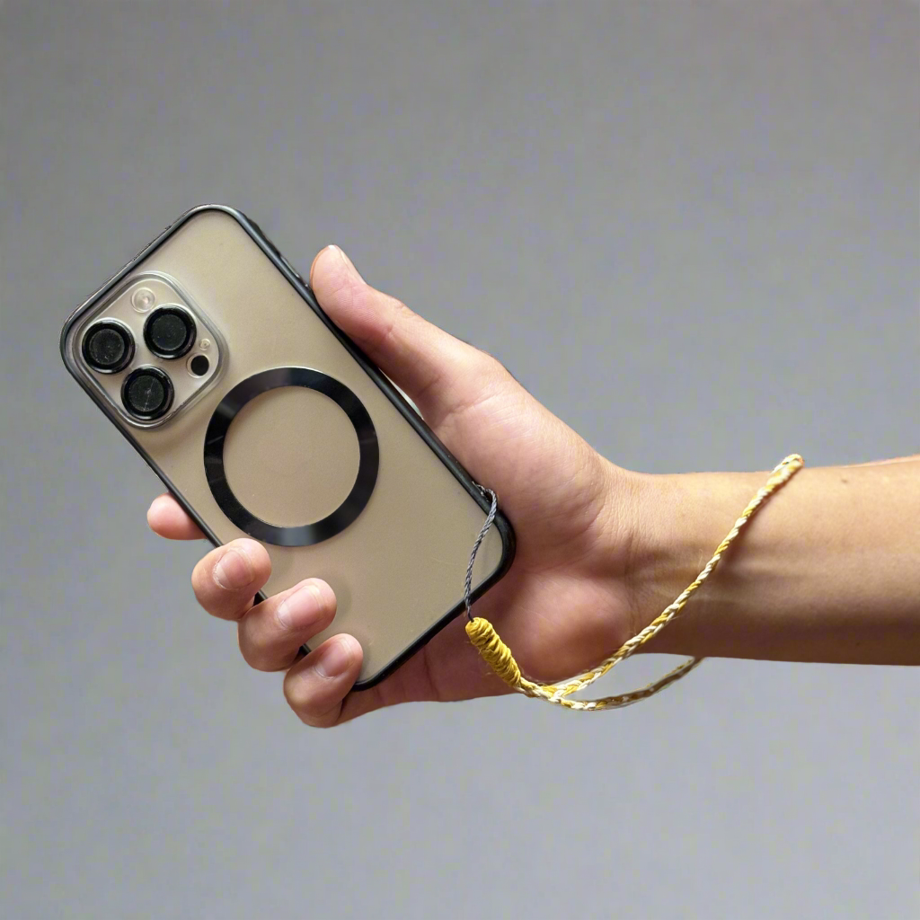 A hand holds a smartphone with a beige case featuring a black circular grip. A yellow wrist strap is attached to the phone, set against a plain gray background.