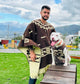 Man and dog, both wearing matching patterned ponchos, stand on grass. The dog sits atop a wooden box, tongues out, in a park with mountains and graffiti in the background.