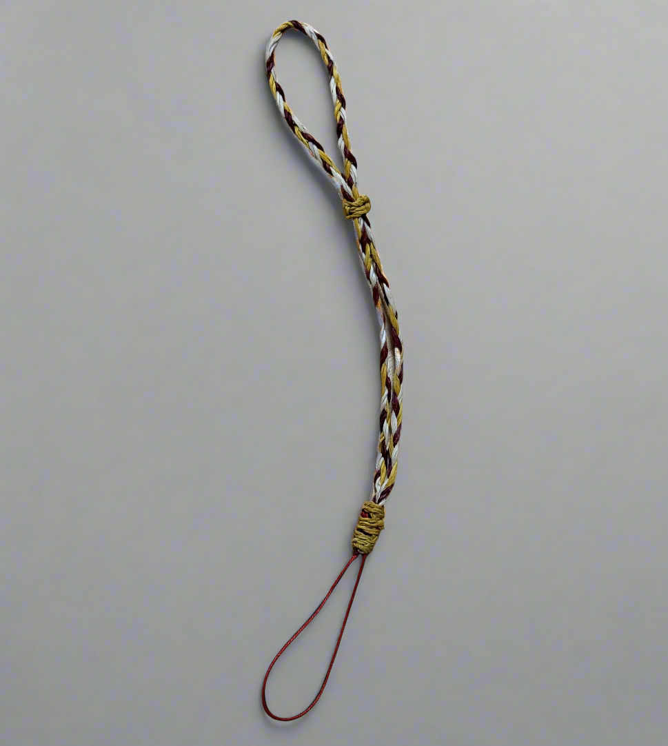 A braided strap forms a loop, featuring intertwined gold, brown, and white threads against a plain gray background.