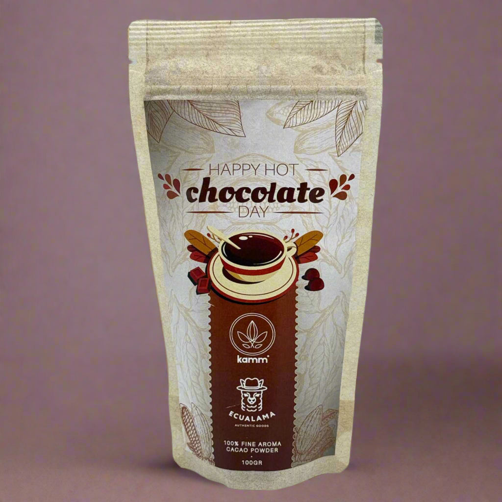 A beige package displays a hot chocolate illustration with surrounding leaves and text: Happy Hot Chocolate Day, Kamm, Ecualama Authentic Goods, 100% Fine Aroma Cacao Powder, 100GR. It's set against a plain background.