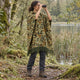 Camo Puyu alpaca wool poncho – woman birdwatching with binoculars by a lake, wearing the sage green, rust and black camouflage hooded poncho