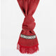 A red scarf is knotted, featuring a black-and-white geometric pattern band and fringe edging, set against a plain white background.