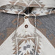 A fabric poncho features a geometric pattern in beige, gray, and white, with wooden buttons and drawstrings at the collar, suggesting a warm, traditional garment.