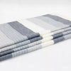 A neatly folded stack of striped blankets, featuring alternating grey and white bands, lies on a plain white surface in a well-lit environment.