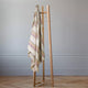 Quijos alpaca wool blanket – a wooden clothes rack holds a striped blanket and a hanger in a minimalist room with light wooden flooring and pale walls