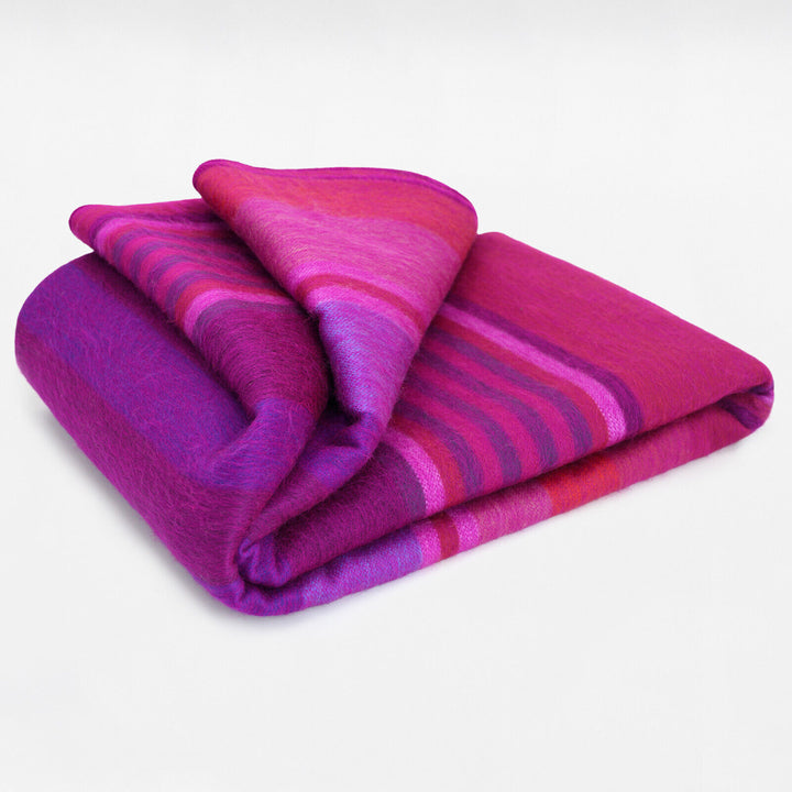 Chone baby alpaca wool blanket – a soft, folded blanket with vibrant purple and pink hues featuring horizontal stripes sits against a plain white background