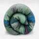 Imbabura baby alpaca wool blanket – a thick, multicolored woolen blanket is tightly rolled, featuring shades of green, blue, and purple, set against a plain white background