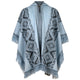 Blue poncho with geometric patterns featuring diamond shapes, lined with fringes; displayed on a plain white background, highlighting its design and texture.