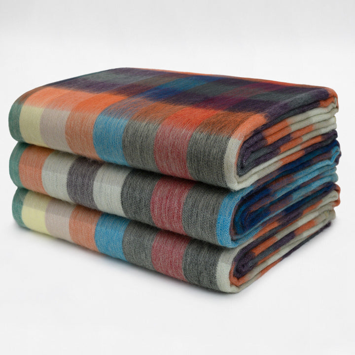 Anzu baby alpaca wool blanket – three stacked, multicolored plaid blankets are neatly folded, placed on a plain white surface, displaying patterns in shades of orange, blue, gray, and cream