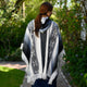 Palora lightweight alpaca wool hooded poncho – a person wearing a patterned poncho walks on a garden path surrounded by lush greenery and flowering plants