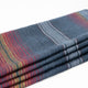 Huasaga baby alpaca wool blanket – a folded woolen blanket rests on a flat surface, featuring red and blue striped patterns. The texture appears soft and fuzzy, enhancing its cozy appearance