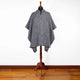 A black-and-white patterned poncho drapes over a wooden mannequin stand, set against a plain white background with a wooden floor.