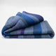 Morona baby alpaca wool blanket – a folded, multicolored blanket featuring blue and purple stripes rests on a plain white surface, creating a calm, neutral background