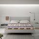 A bed with patterned bedding and white pillows is in a modern bedroom. A bedside table holds a lamp and mug, with an alarm clock showing 10:00 nearby on another table.