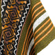 A textile displays geometric patterns with diamond shapes in warm tones, bordered by olive green, orange, and white stripes, creating an intricate design.