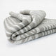 A thick, folded, patterned blanket with beige and white stripes rests on a plain, white surface.