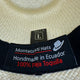 A woven hat features a label displaying, Montecristi Hats, Handmade in Ecuador, 100% paja Toquilla, with a hat icon. A small tag above reads TALLA L indicating size.