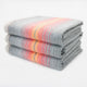 Ajilanga baby alpaca wool blanket – three stacked gray blankets, featuring a vibrant pattern of red, orange, pink, and yellow stripes, are placed against a plain white background