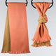 Two scarves hang on black rings. The left scarf is peach and olive, hanging straight. The right scarf is knotted, showing peach and olive colors, with fringed ends. Neutral background.