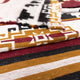 Textiles overlap, featuring geometric patterns in black, white, mustard yellow, and maroon. The top fabric has a fringe edge. The context is a close-up view.