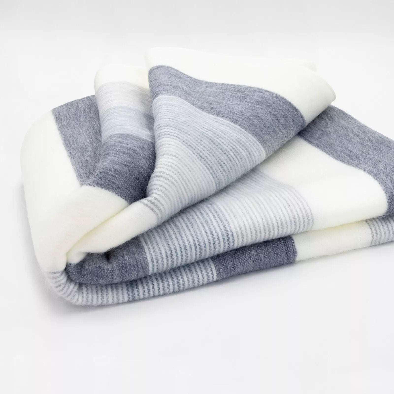 A folded, striped blanket with gray and white horizontal bands, resting on a plain white surface, creating a soft and cozy appearance.