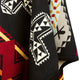 A textile piece displays intricate geometric patterns and shapes in black, white, red, yellow, and light blue, creating a traditional or cultural aesthetic. The fabric appears layered and draped.