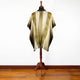 A tan and yellow patterned poncho is displayed on a wooden mannequin stand, situated on a polished wooden floor against a plain white wall.