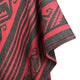 A piece of fabric, adorned with red and black geometric patterns, hangs or drapes in an undefined space, showcasing intricate, angular designs and vibrant contrast.