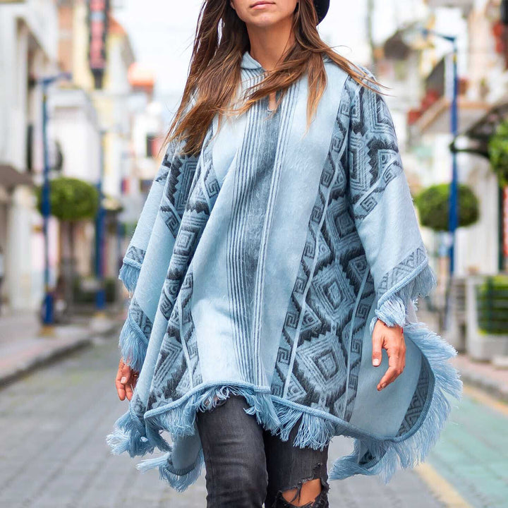 A person wearing a patterned blue poncho walks along a city street. The background features blurred buildings and greenery, suggesting an urban setting bustling with activity.